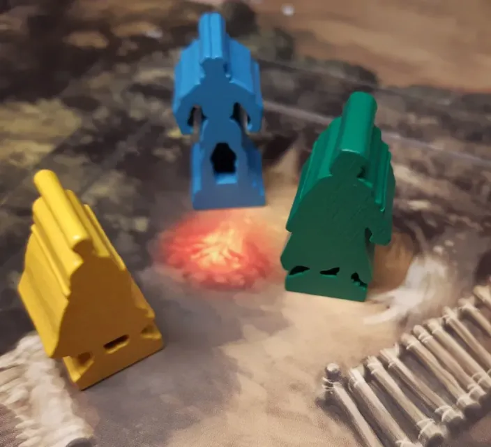 Tres figuras de madera de colores, amarilla, azul y verde, junto a una hoguera en el mapa del bosque.