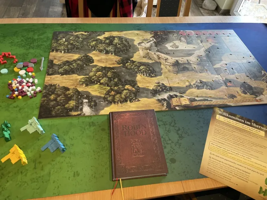 Mapa grande de Nottingham y el bosque de Sherwood montado en una mesa, con el libro de aventuras delante y las fichas de colores a un lado.